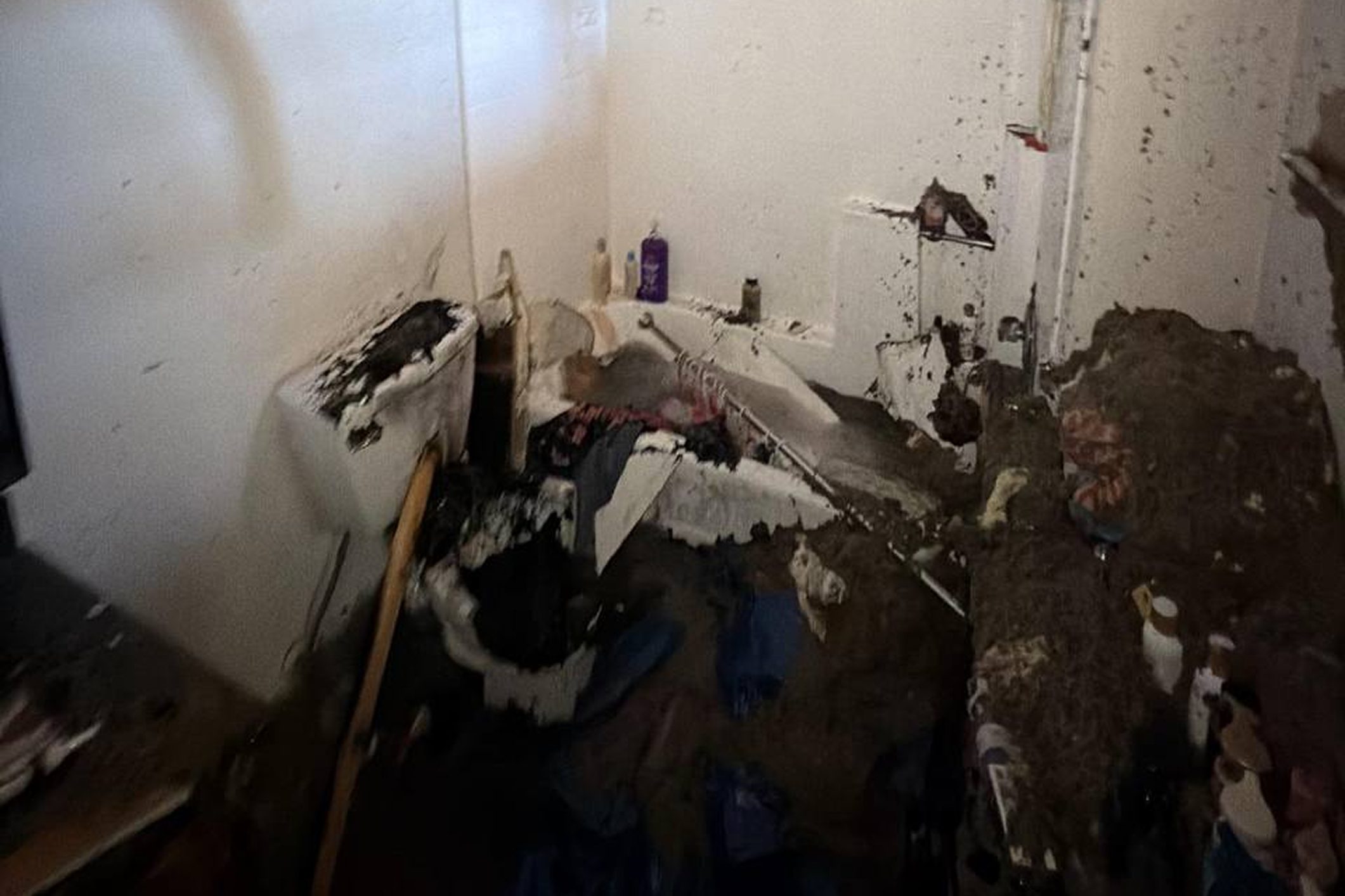 Flood-damaged bathroom filled with mud and debris