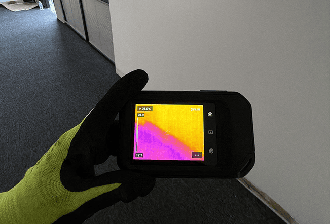 Gloved hand holding thermal camera at wall corner