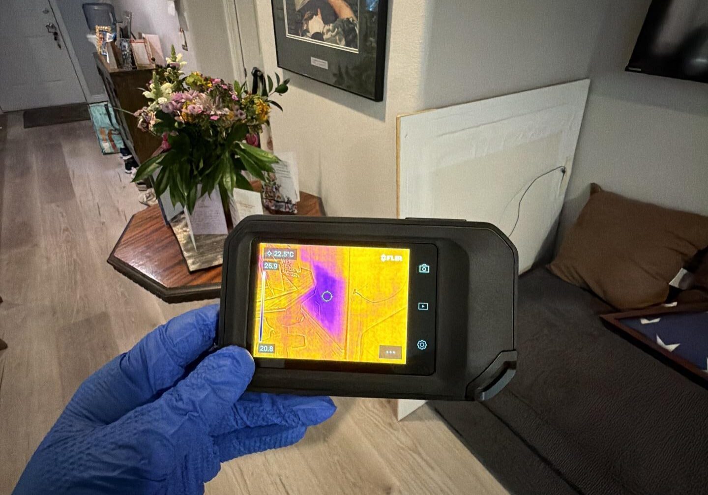Gloved hand holding thermal camera in living room